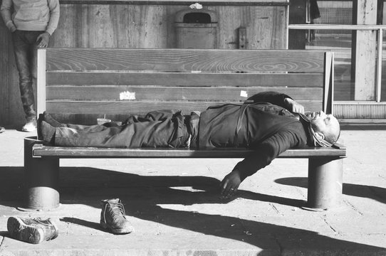 Homeless man, Poor homeless man or refugee sleeping on the wooden bench on the urban street in the city, social documentary concept, selective focus, black and white