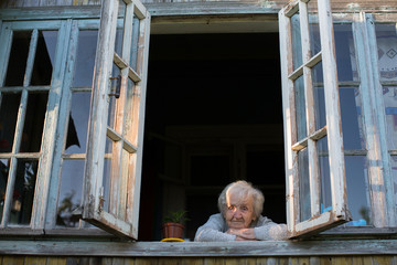 An elderly woman looks out of the window of a village house.