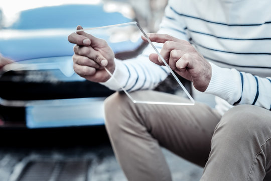 Technological progress. Close up of an innovative tablet being in hands of a cheerful positive man while sitting near his car