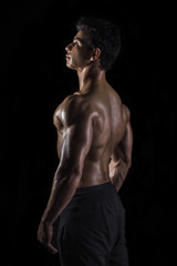 Fototapeta na wymiar Highly retouched fitness model and bodybuilder. Posing his back muscles. looking high. concept of self-confidence and power. black background.