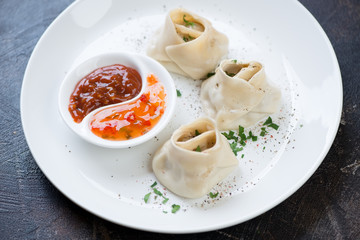 White plate with steamed meat dumplings manti and two types of sauces, studio shot, selective focus
