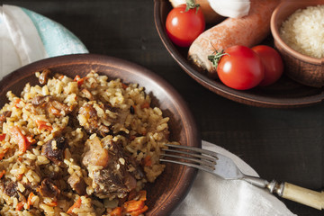 Plov and ingredients in a plate on a dark wooden background.