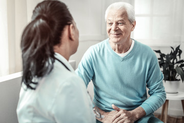 Consulting conversation. Senior gray hair pleasant man sitting in the room and looking at the doctor and smiling.
