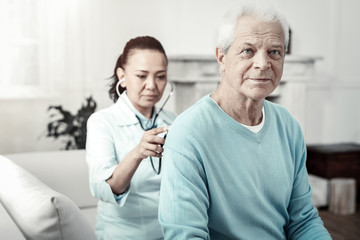 Fototapeta premium Relax and breathe. Aged pleasant concentrated man sitting in the room on the sofa doing nurses orders and looking aside.
