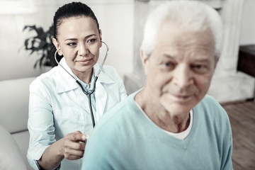Fototapeta premium Qualified doctor. Young kind cute nurse sitting behind the patient examining him and smiling.