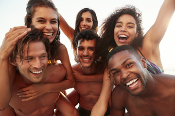 Obraz premium Group Of Friends On Vacation Having Piggyback Race On Beach