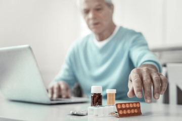 Its for me. Aged senior serious man sitting by the table holding hand near pills and trying to keep tablets.
