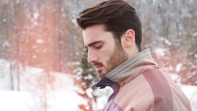 Handsome young man in skiing suit relaxing, using cell phone to make a call, standing outside at ski resort