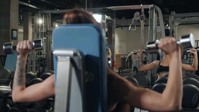 Brutal athletic woman pumping up muscules with dumbbells, training girl with barbell in gym indoor