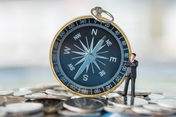 Business and planning concept. Businessman miniature figure standing on pile of coins with compass as background.