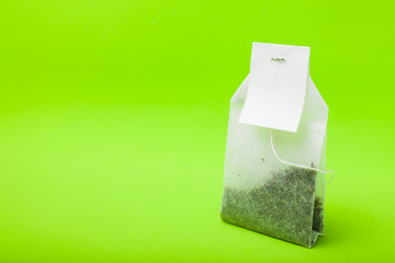 A new tea bag on a green background. Copy space, mockup.