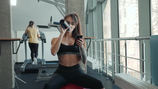 Young athletic woman drinking water in gym after hard workout .