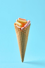 Pink and yellow Marshmallows in waffle cone on light blue background. Free space for your text