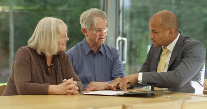 4K Cheerful senior couple signing a document in a meeting with financial adviser. Slow motion