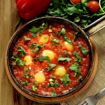 Fried eggs with tomato sauce and parsley in a cast iron pan. Shakshuka a traditional meal of the Jewish cuisine