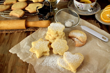 Shaped shortbread cookies covered with sugar powder surrounded by kitchen utensils