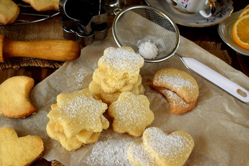 Shaped shortbread cookies covered with sugar powder surrounded by kitchen utensils