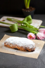 freshly baked cake with sweets, raisins and candied fruits, sprinkled with powdered sugar on a gray table with pink tulips