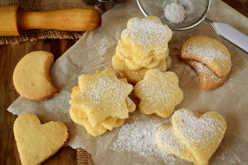 Shaped shortbread cookies covered with sugar powder surrounded by kitchen utensils