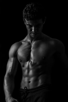 Highly retouched black and white fitness model and bodybuilder, Looking and posing abs and chest. concept of power, strength and self-confidence. black background.