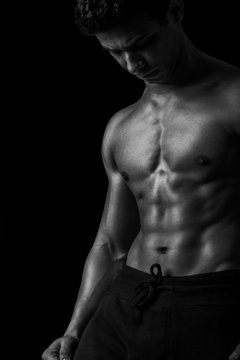 Highly retouched black and white fitness model and bodybuilder, Looking and posing abs and chest.  concept of power, strength and self-confidence. black background.