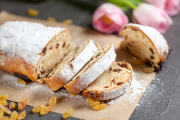 freshly baked cake with sweets, raisins and candied fruits, sprinkled with powdered sugar on a gray table with pink tulips