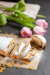 freshly baked cake with sweets, raisins and candied fruits, sprinkled with powdered sugar on a gray table with pink tulips