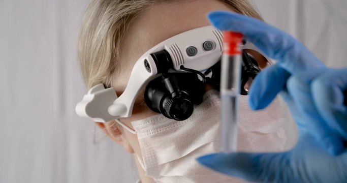Laboratory work, a woman doctor holds a test tube, in a medical mask and professional glasses, a magnifying glass, takes an analysis from a test tube in blue rubber gloves, analysis, blood, DNA, a tes