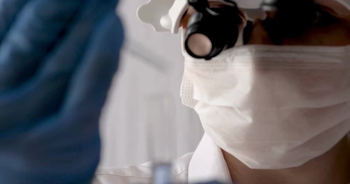 Laboratory work, a woman doctor holds a test tube, in a medical mask and professional glasses, a magnifying glass, takes an analysis from a test tube in blue rubber gloves, analysis, blood, DNA, a tes