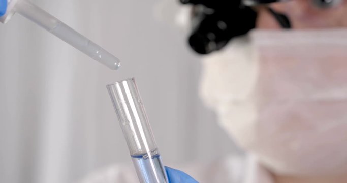 Laboratory work, a woman doctor holds a test tube, in a medical mask and professional glasses, a magnifying glass, takes an analysis from a test tube in blue rubber gloves, analysis, blood, DNA, a tes