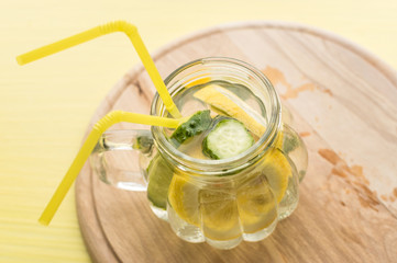 water with lemon and cucumber on a wooden board and yellow background
