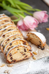 freshly baked cake with sweets, raisins and candied fruits, sprinkled with powdered sugar on a gray table with pink tulips