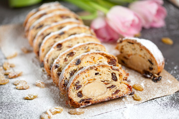freshly baked cake with sweets, raisins and candied fruits, sprinkled with powdered sugar on a gray table with pink tulips