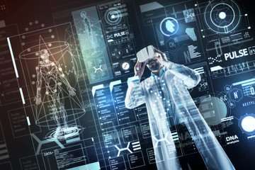Futuristic medicine. Qualified emotional young doctor wearing amazing virtual reality glasses and...