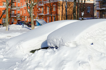 Fototapeta premium Parked cars under snowdrifts in city yard after snowfall in March