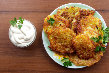 Homemade fried potato pancakes with sour cream on wooden table