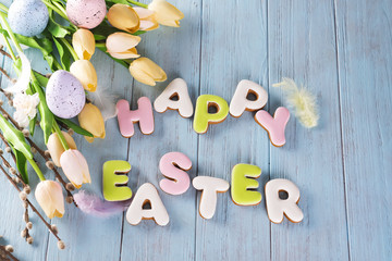 Easter cookies letter Happy Easter and colorful eggs with tulips on wood background