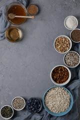 Ingredients for cooking homemade granola: oatmeal, raisins, coconut chips, honey, peanuts, cocoa, blueberries, vegetable oil, flax, sesame, pumpkin and sunflower seeds. Concrete background. Top view.