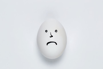 The hen of the white egg is painted with a sad face. on a white background