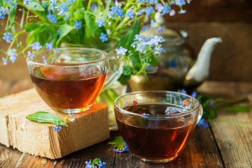 Tea cup, teapot, honey jar and summer bouquet of blue cornflowers on table outdoors. Summer still life.