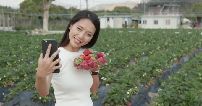 Woman taking selfie with cellphone after picking strawberry field