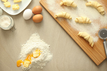 Wooden board with raw croissants and ingredients on table