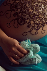 Mehendi artist paints an ornament of mandala with henna on an pregnancy woman’s belly