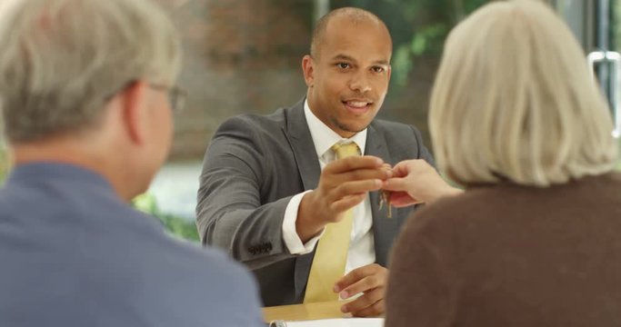 4K Attractive mixed race real estate agent closing a deal with senior couple & giving them key to their new home. Slow motion
