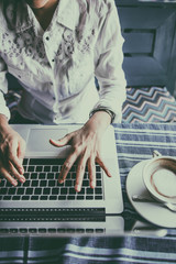 Happiness Asian woman sitting using laptop and mobile  in a cafe.
Focus on hand