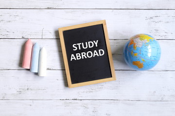 Top view of globe of world map,chalk and blackboard written with ' STUDY ABROAD' on white wooden background.