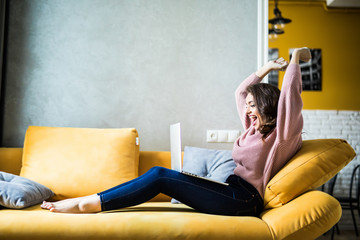 Young woman raising her hands up on the couch with laptop at home