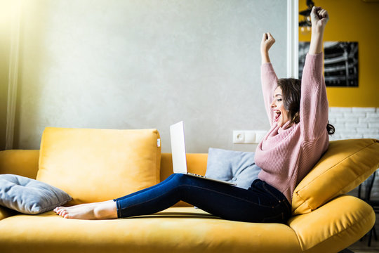 Pretty young woman using a laptop while raising hand and sitting on the couch