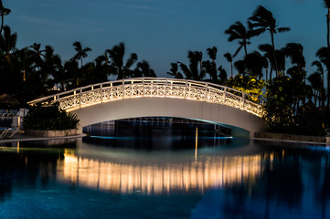 Long exposure of an illuminated foot bridge over a swimming pool as dawn breaks.