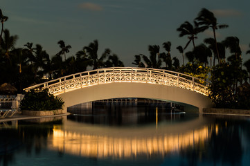 Long exposure of an illuminated foot bridge over a swimming pool as dawn breaks.